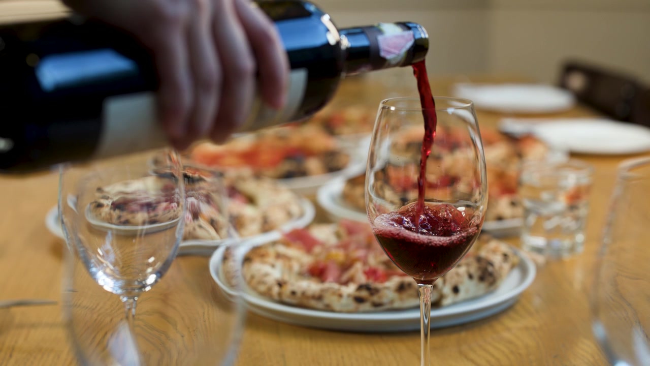 Primo piano di vino rosso versato in un bicchiere accanto a pizza fresca su un tavolo di ristorante