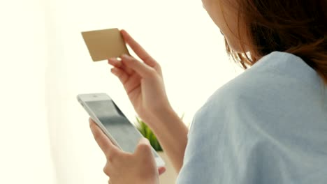 close up young asian young woman smiling with smartphone and credit card beside the window at home. beautiful woman shopping online with credit card.