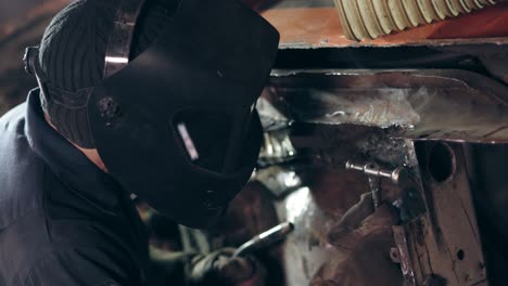 male worker at a welding factory in welding mask uses hammer to fixate piece of metal on unidentified construction. welding on