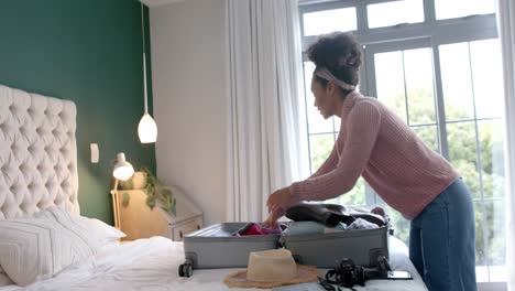 biracial woman packing suitcase in sunny bedroom, slow motion