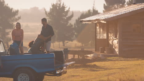 group of friends unloading backpacks from pick up truck on road trip to cabin in countryside