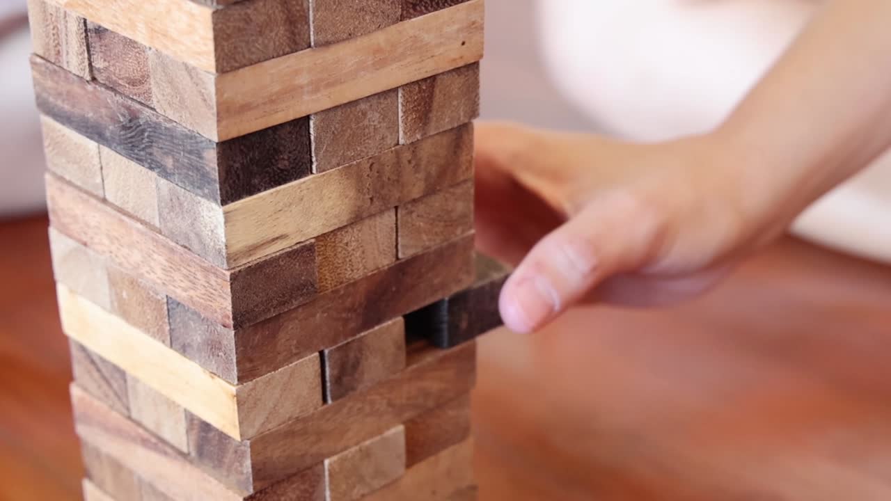 Mão removendo cuidadosamente um bloco de madeira de uma torre, demonstrando precisão, foco e equilíbrio.