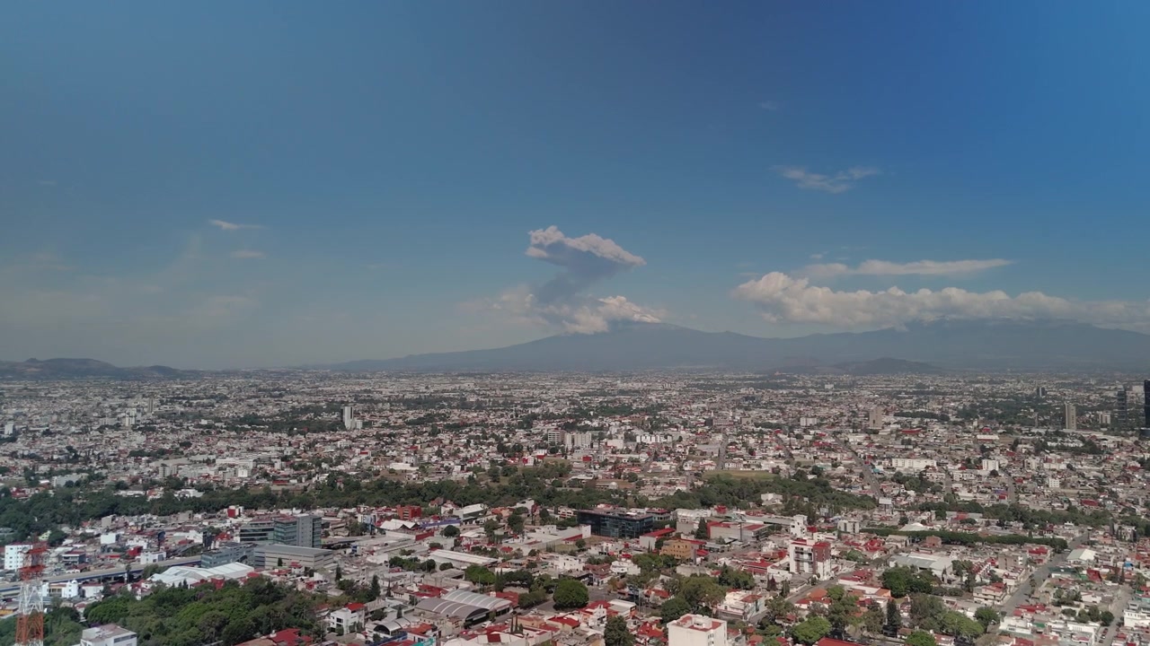 Vista panoramica della città di Puebla con il maestoso vulcano Popocatépetl che si erge in lontananza e rilascia fumo vulcanico. Un paesaggio messicano visivamente accattivante che combina architettura urbana e elementi naturali.