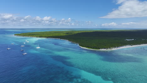 Descending-drone-shot-of-a-beachfront-in-the-island-of-the-Dominican-Republic,-showing-the-yachts-and-the-scenic-coastline-in-the-Caribbean-island