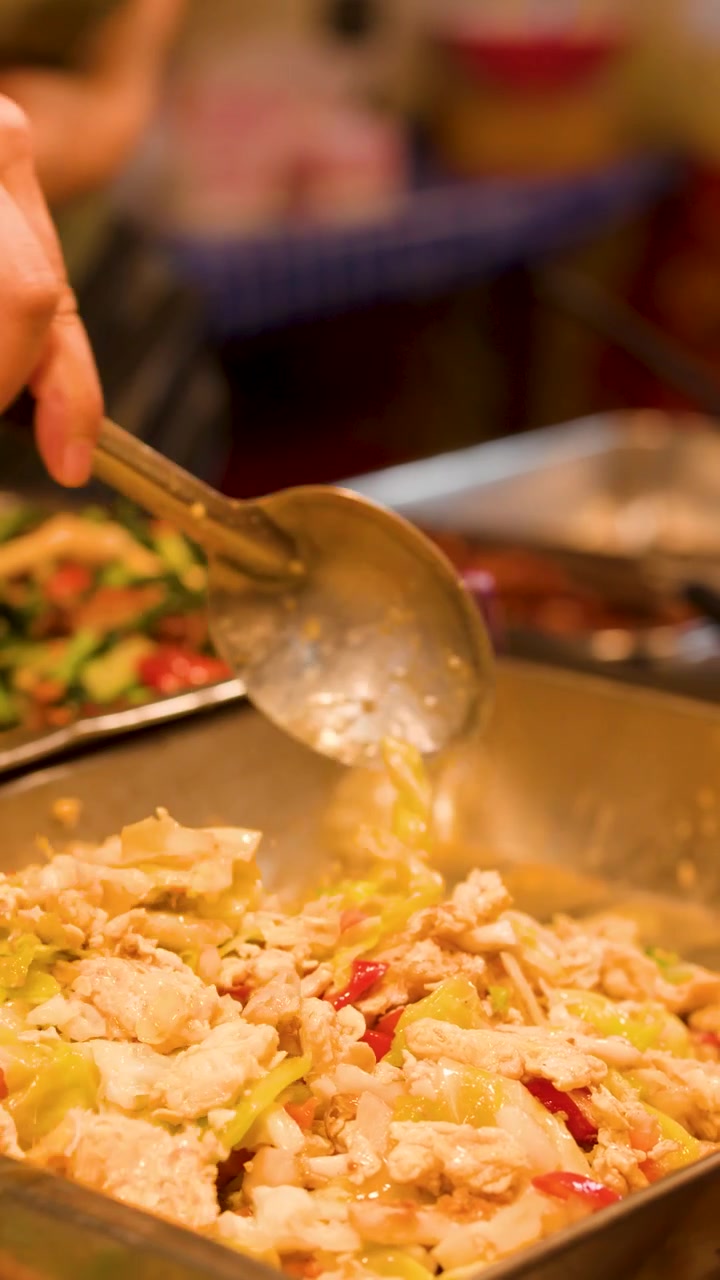Nærbillede af en sælger, der bruger en metalske til at servere lynstegt kål fra buffetbakker