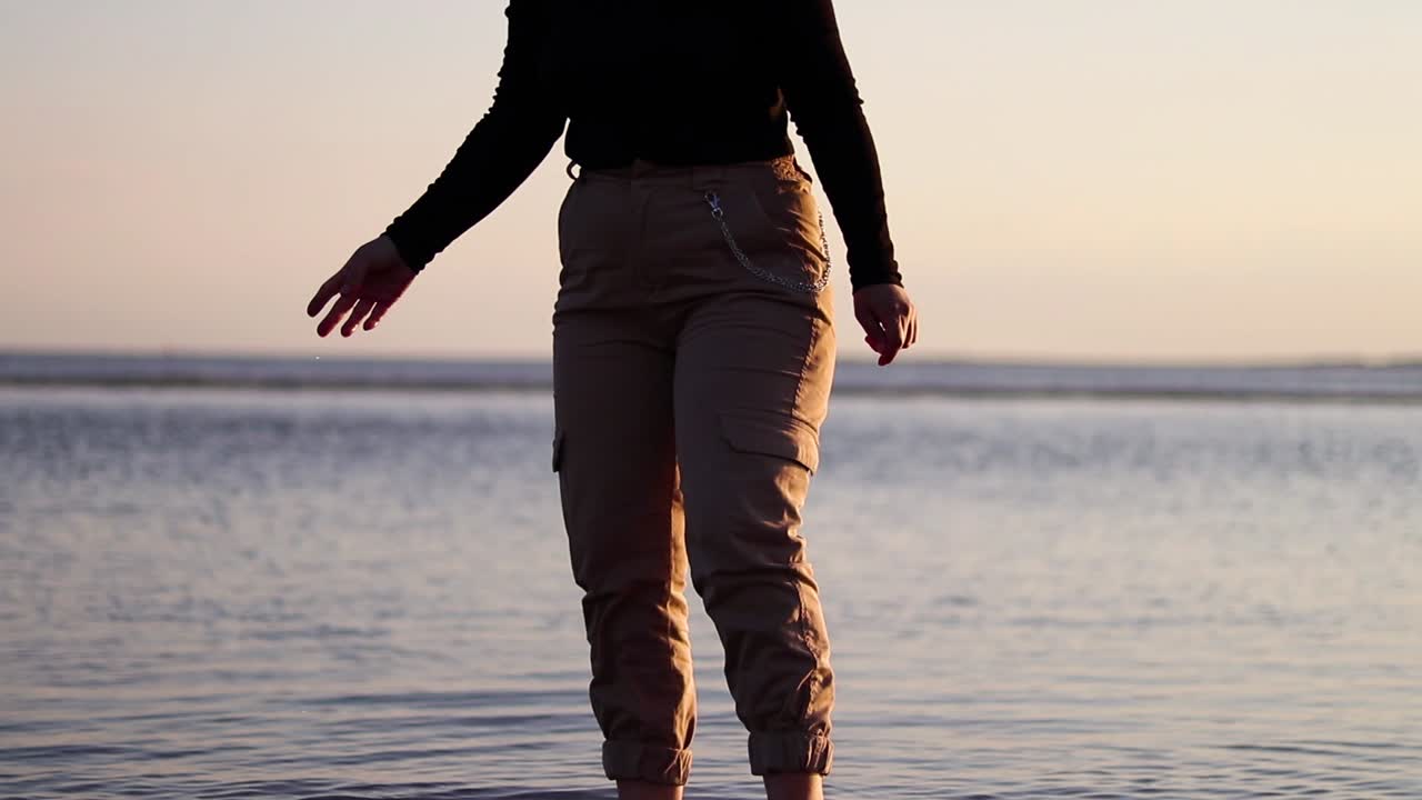 석양에 바다 옆 진흙에서 그녀의 발을 청소하는 소녀