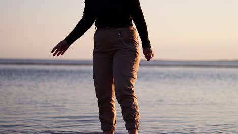 girl cleaning her feet from the mud by the sea at the sunset