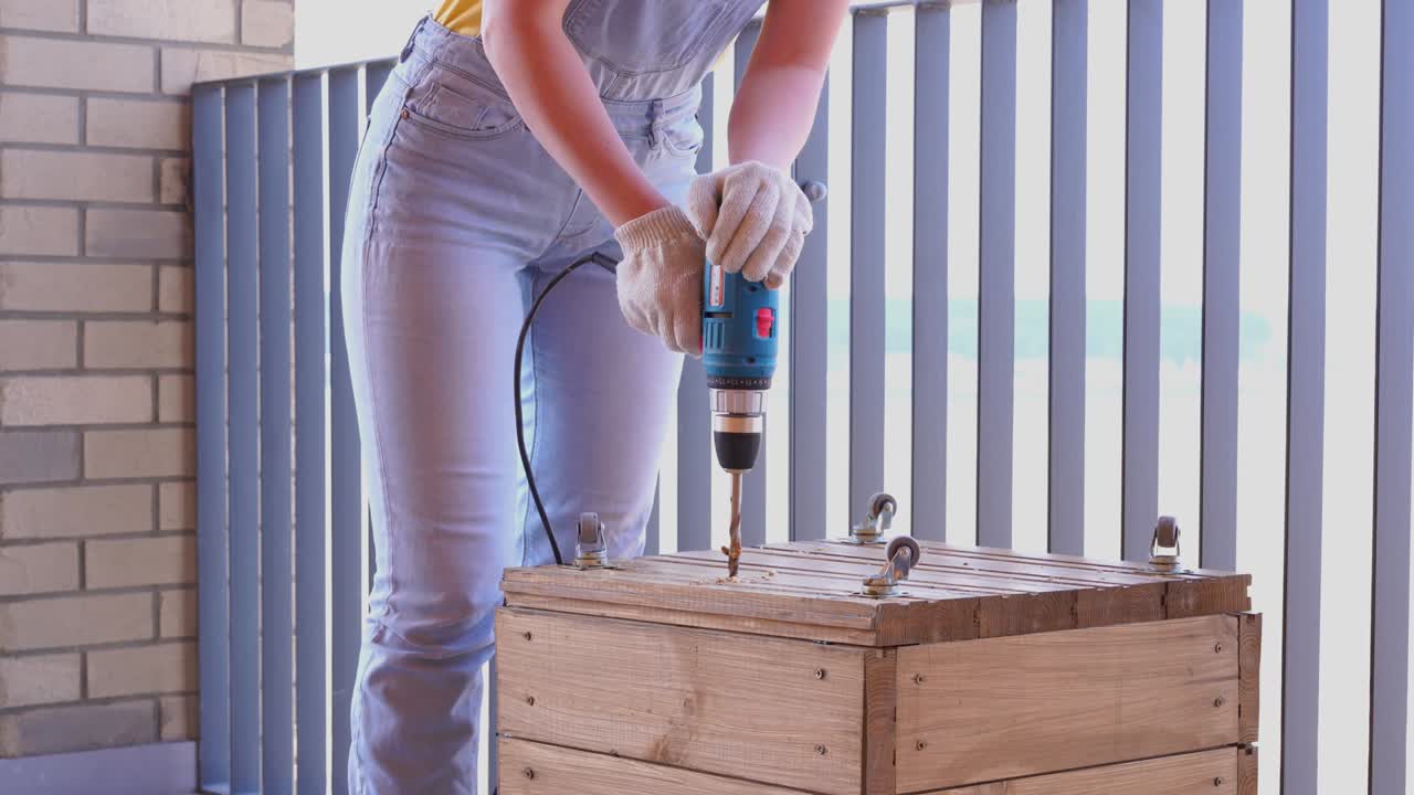 una mujer en una terraza hace un trabajo no femenino - perfora un agujero con un destornillador en una caja de madera