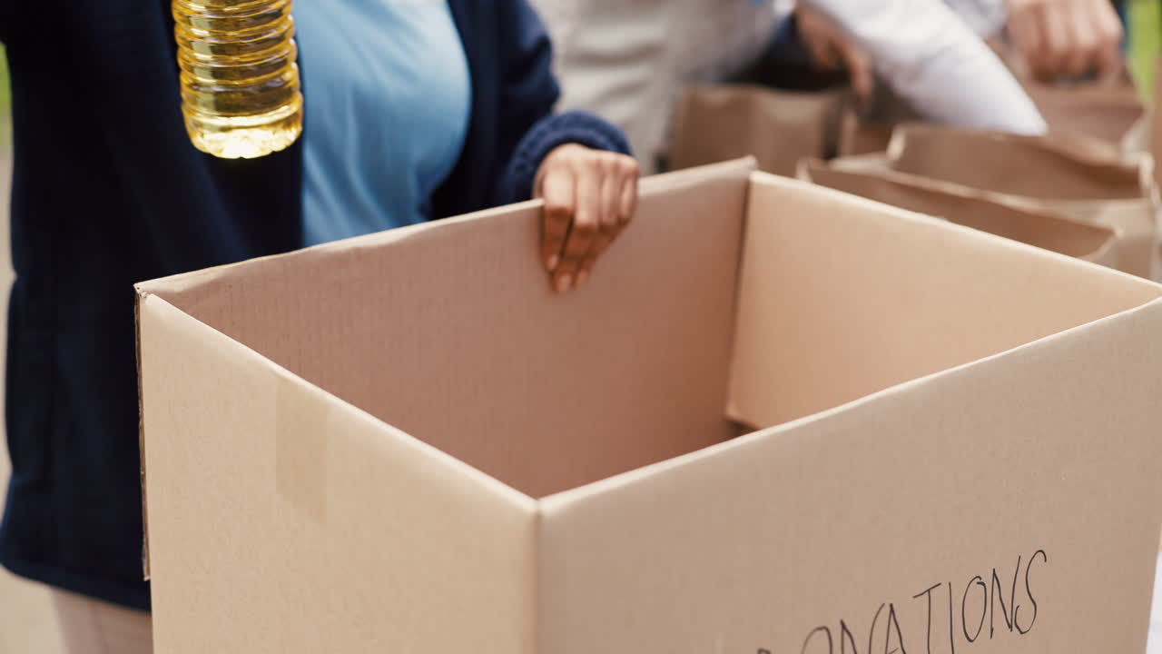 Person Placing Food Items into a Cardboard Donation Box