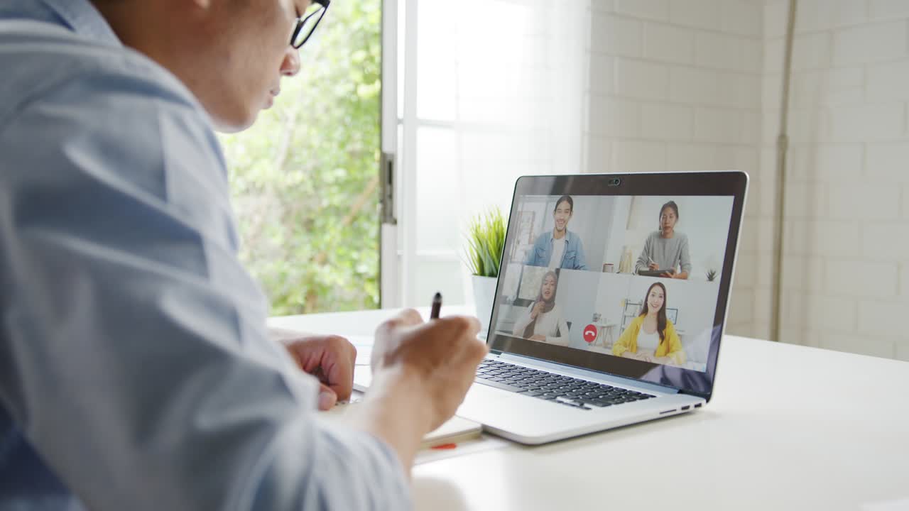 アジアの若いビジネスマンがラップトップを使って自宅のリビングで仕事をしている間ビデオコールで会議の計画について同僚と話します