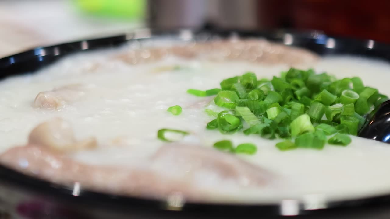 A detailed view of creamy rice porridge topped with fresh green onions in a black bowl.