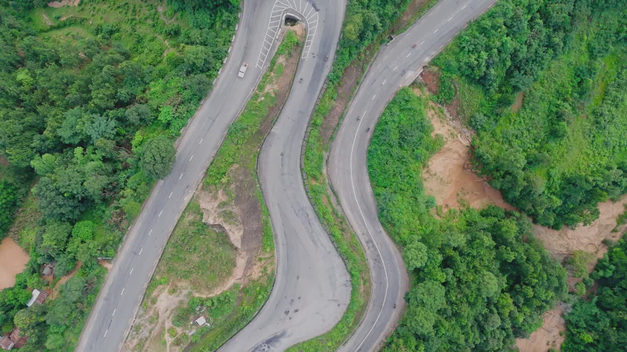 Aerial view of a vehicle driving along a winding hillside road surrounded by lush green mountains, showcasing scenic mountain travel, nature, and rural transportation beauty