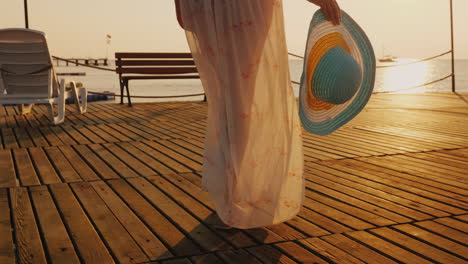 een vrouw loopt over de pier richting de rijzende zon op de foto zie je een hand met een hoed reizen