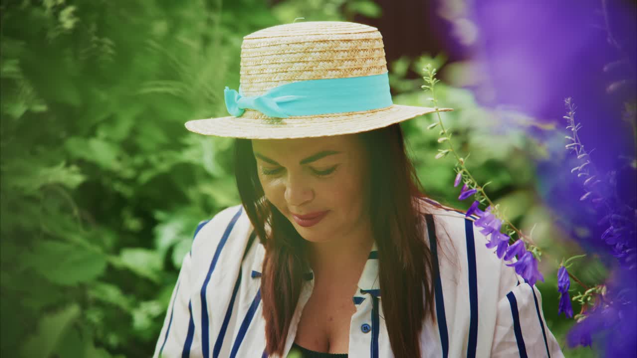 Woman in straw hat examining flowers in a vibrant garden surrounded by lush greenery and blooms