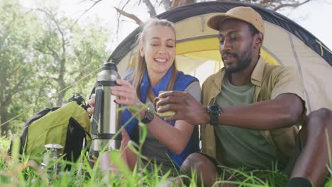 Happy-diverse-couple-camping-and-drinking-tea-in-park,-slow-motion