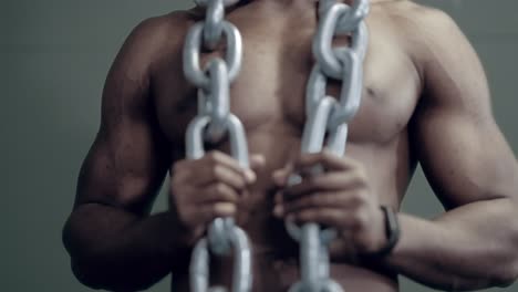 a muscular african male stands with weight chain for dips