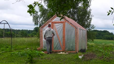 Statische-Aufnahme-Eines-Bauern,-Der-Im-Garten-Durch-Ein-Gewächshaus-Mit-Plastikfolie-Geht