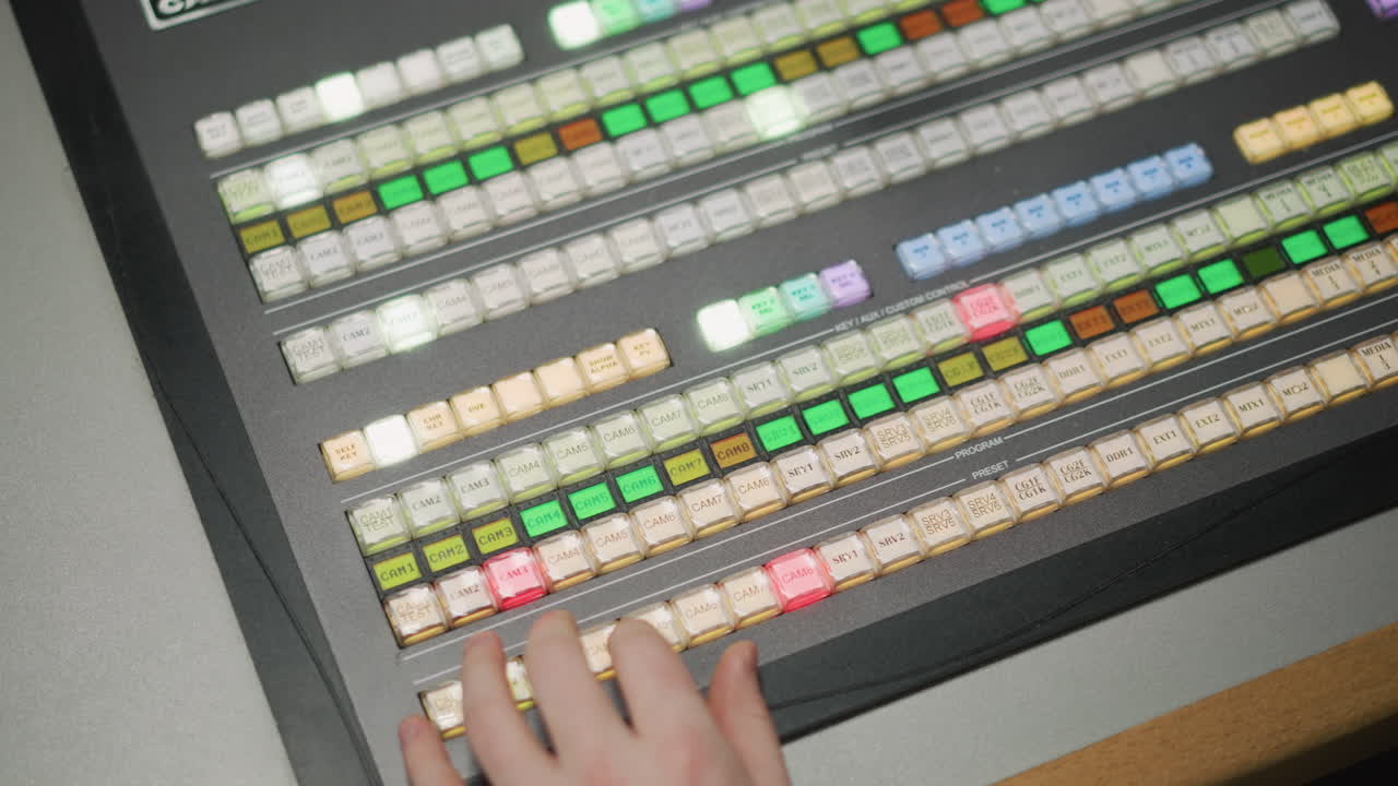 Close-up view of television broadcast control panel with multiple buttons and lights being operated by hand, showing camera controls and transitions during live production or broadcast event