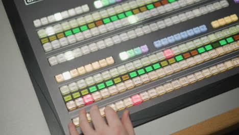 close-up view of television broadcast control panel with multiple buttons and lights being operated by hand, showing camera controls and transitions during live production or broadcast event