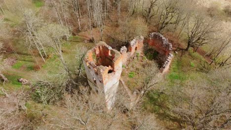 Droning over red brick ruins of old church in Latvian woodland during spring