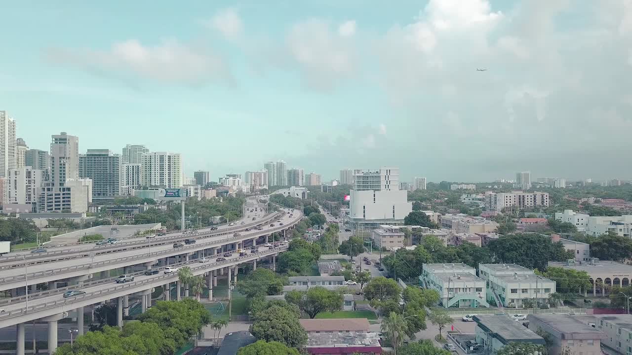 Miami traffic with buildings and a plane flying in the background on a sunny day with clouds
