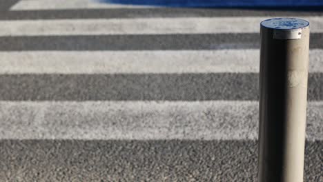 Close-up-of-a-vertical-pole-marking-a-crosswalk-where-multiple-vehicles-are-circulating