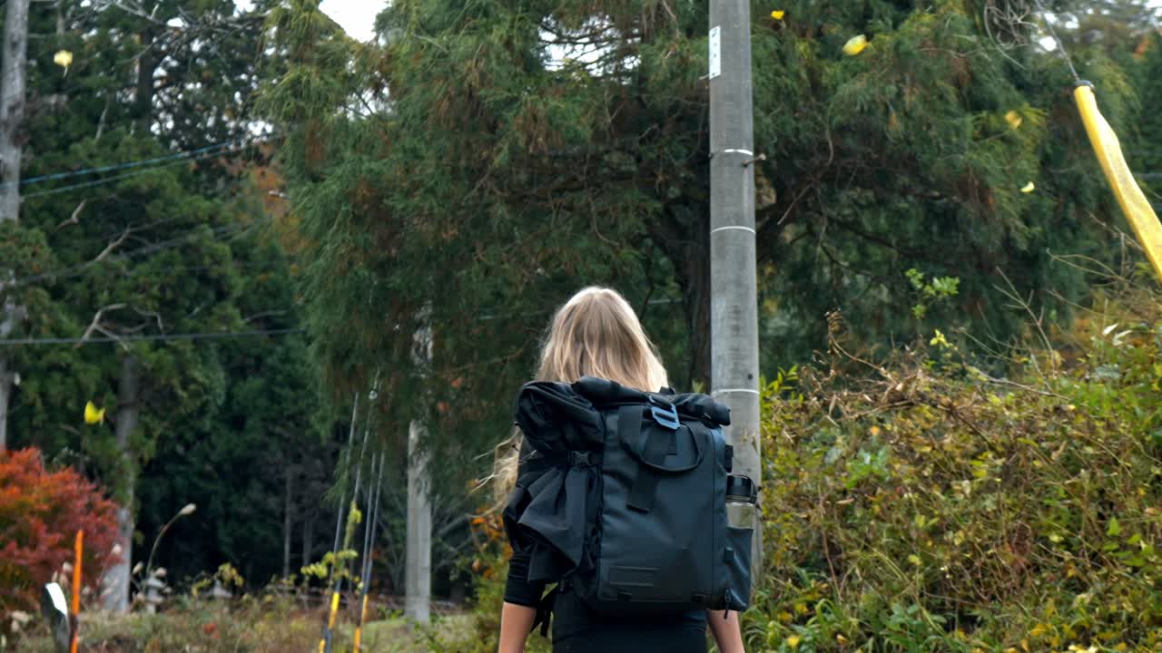 A peaceful moment as a woman walks along the historic Nakasendo Trail in Japan, surrounded by vibrant autumn colors and falling leaves.
