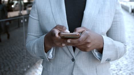 primer plano de una empresaria afroamericana irreconocible parada afuera y escribiendo un mensaje de texto en el teléfono celular