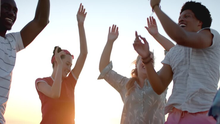 Un gruppo eterogeneo di amici festeggia, alzando le mani contro un cielo al tramonto.