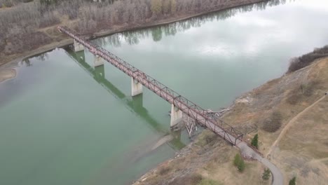 1-3 vista de pájaro volar sobre el puente de armadura marrón de los niños peatonales en el parque sobre un río contaminado en el otoño sin nadie a la vista aceptar una casa de castores al pie del puente un ganso canadiense junto a él