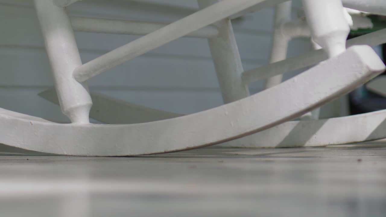 cámara lenta silla de balanceo de madera blanca en el porche balanceándose hacia adelante y hacia atrás pacíficamente