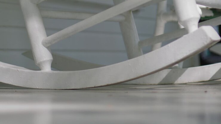 Sedia a dondolo in legno bianco in slow motion su un portico che dondola avanti e indietro pacificamente