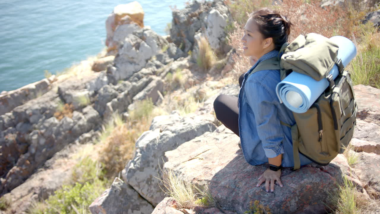 Hiking in mountains, woman with backpack and yoga mat resting on rock
