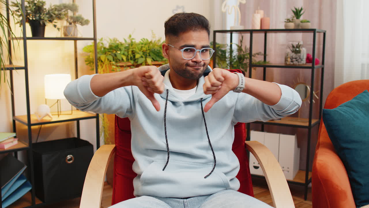 Upset arabian man showing thumbs down dislike bad work disapproval dissatisfied feedback at home