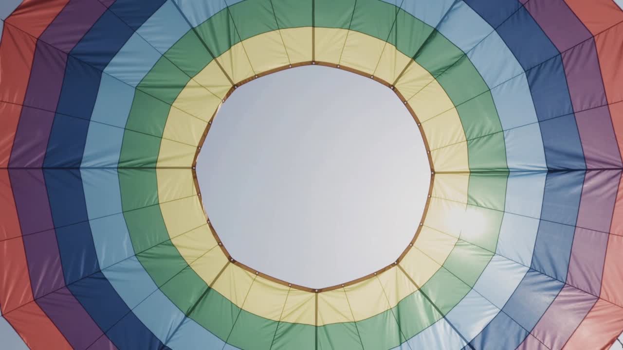 La vela di un pallone aerostatico si sta gonfiando, tendendo i pannelli verso il cielo blu in preparazione al volo, e mostra la valvola di sfogo sulla sommità.