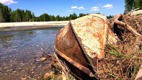 a rusty old drift boat laying on the river bank of the bitterroot river