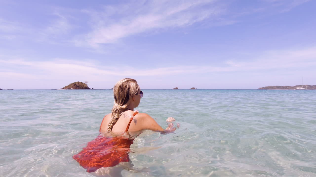 젊고 아름다운 여성은 필리핀 엘 니도에 있는 나판 해변의 맑고 투명한 바다에 앉아 카메라가 둥글고 완벽한 휴가와 꿈의 목적지로 돌아갑니다.