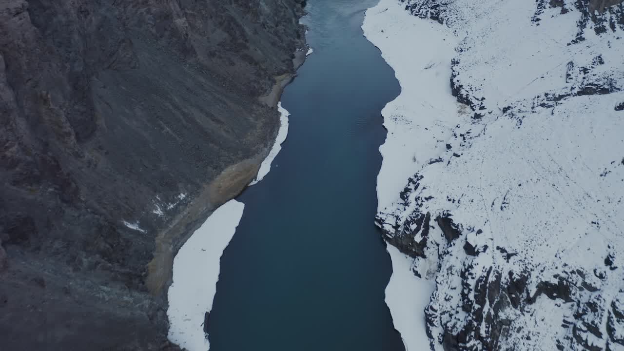 Il fiume Indo attraversa un terreno innevato nella Valle di Leh, Ladakh, durante la stagione invernale. Una veduta aerea a volo d'uccello cattura il contrasto tra la montagna scura, l'acqua e le rive di ghiaccio bianche
