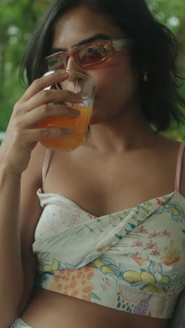 young woman sipping orange drink, relaxed summer vibe, wearing sunglasses outdoors