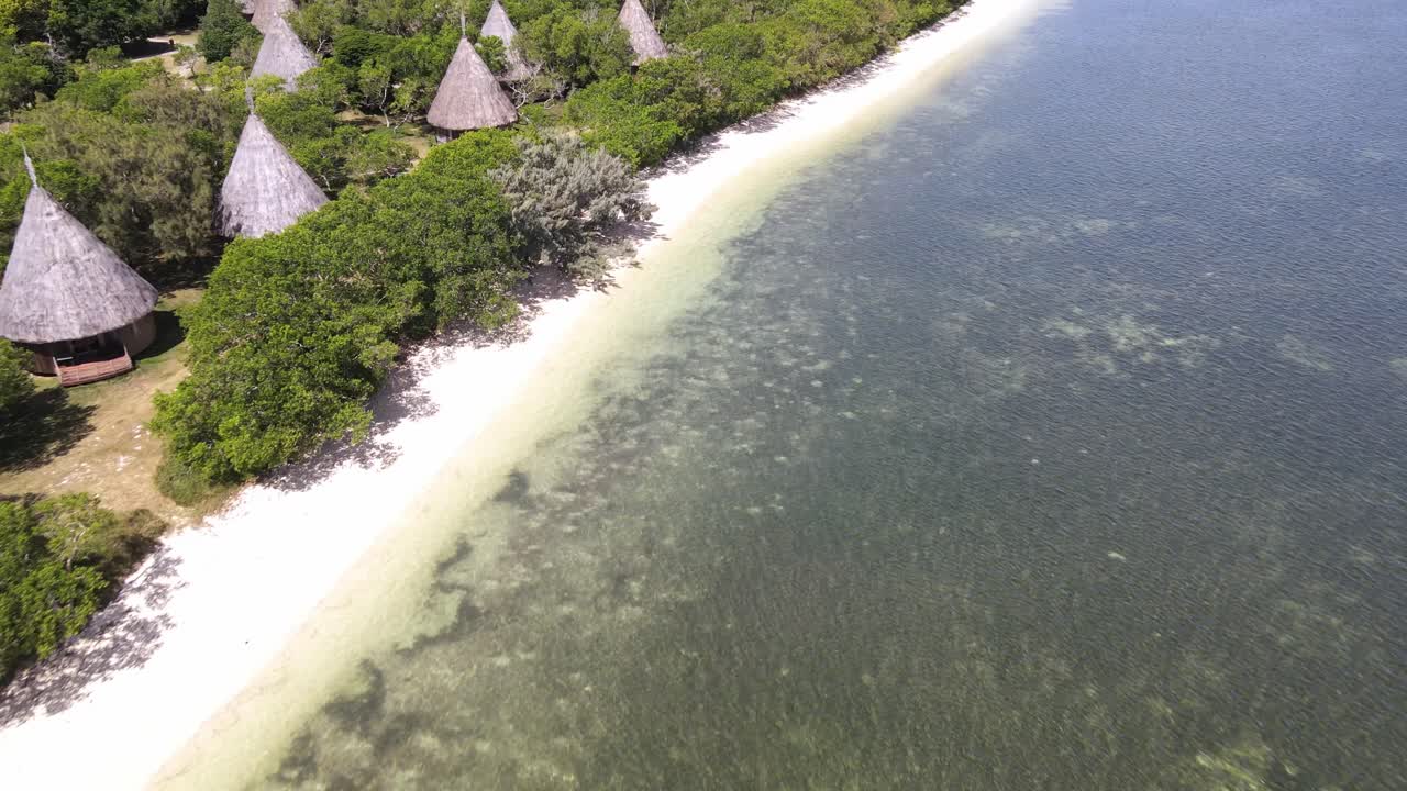 Drone aerial moving down towards a beach in New Caledonia with huts