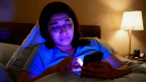 woman using phone in bed at night