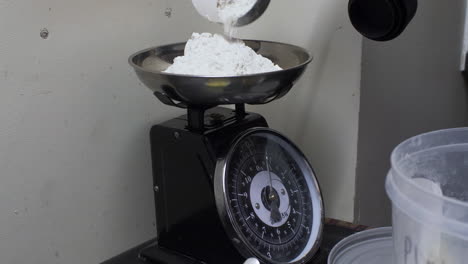 weighing flour from measuring cup on scales on kitchen table