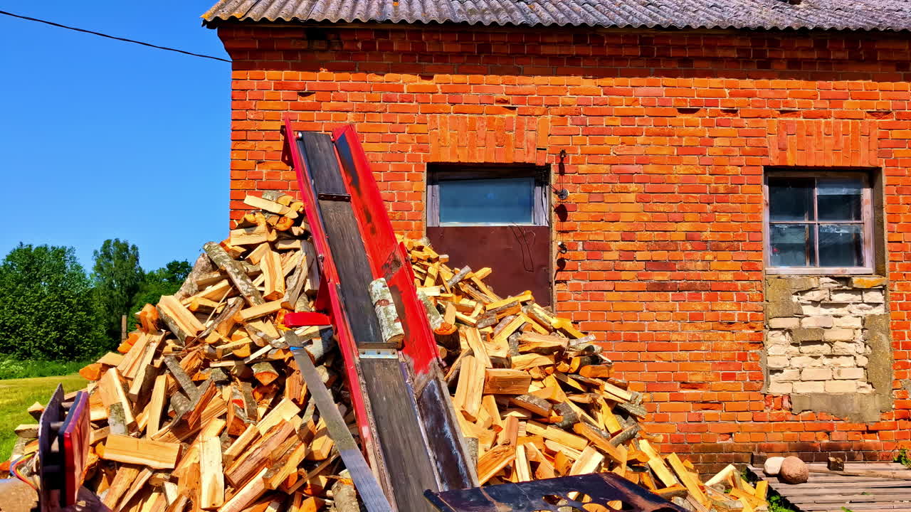 Freshly split firewood stacked near old red brick building and transported on red conveyor lift