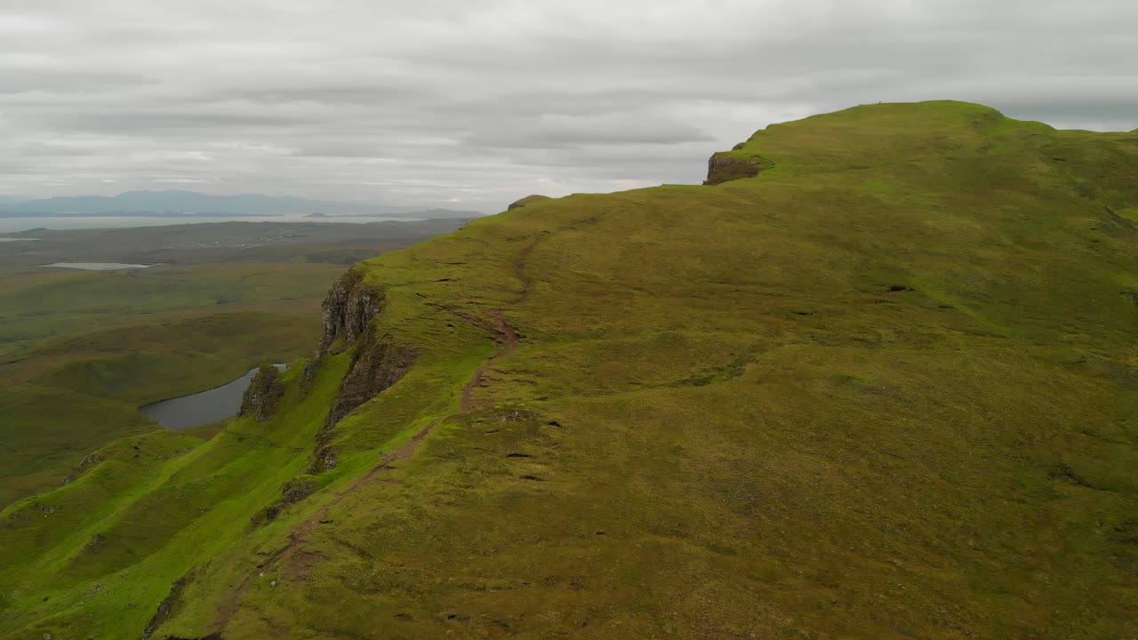 Forward aerial shot of a lush green ridge in Scotland during an overcast day.