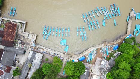 Top-view-of-blue-traditional-outrigger-fishing-boats-lined-up-at-dock,-Baron-Beach,-Indonesia