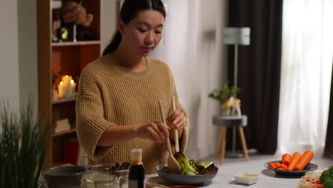 close up of woman at home in kitchen preparing healthy vegetarian or vegan meal mixing salad leaves into bowl