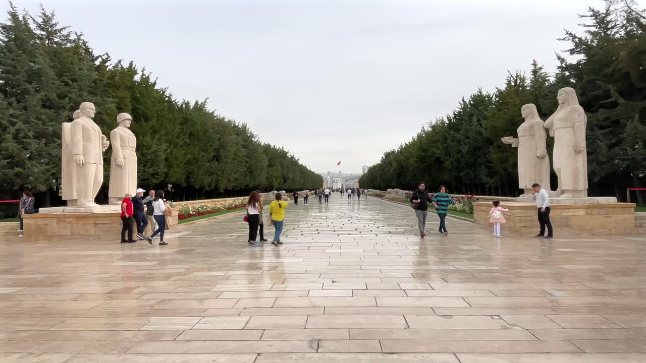 Turkey,Ankara, Ataturk's Mauseloum on a cloudy day. Entrance of the road with lions, at the entrance 3 men's statues on the left and 3 women's statue on the right, People standing and walking around,