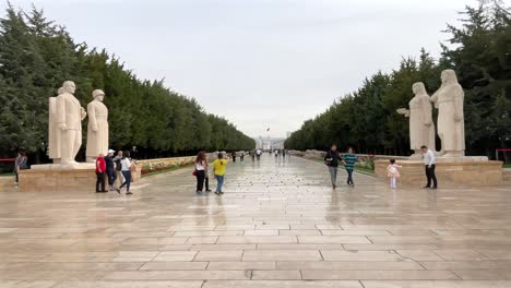 turkey,ankara, ataturk's mauseloum on a cloudy day. entrance of the road with lions, at the entrance 3 men's statues on the left and 3 women's statue on the right, people standing and walking around,