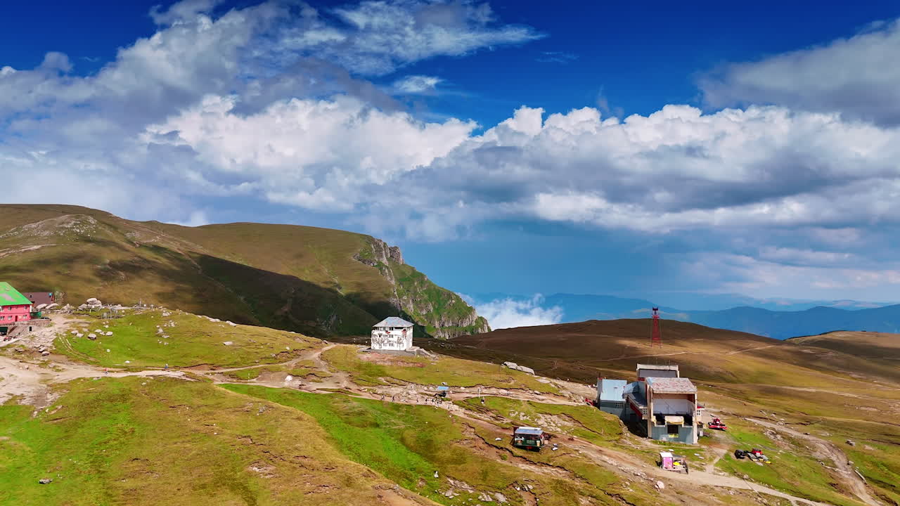 Vista panoramica di un paesaggio montano con edifici e cielo azzurro in estate. Le montagne presentano erba verde ed edifici sotto un cielo azzurro con nuvole durante il giorno in estate.