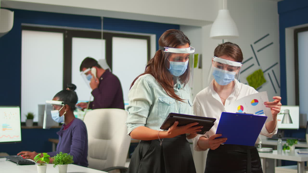 Coworkers with face visor in new normal office comparing graphs